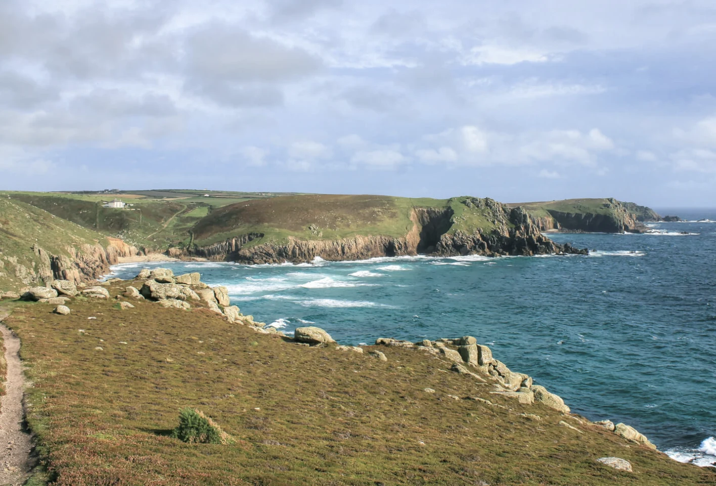 Placeholder photo: the Cornish coast path along granite cliffs, overlooking a turquoise bay and a rocky headland